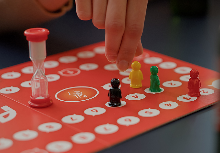 Young people playing charades board games with figurines, rolling dices for cards game. Men and women enjoying strategy competition to guess card for entertainment and fun. Close up.